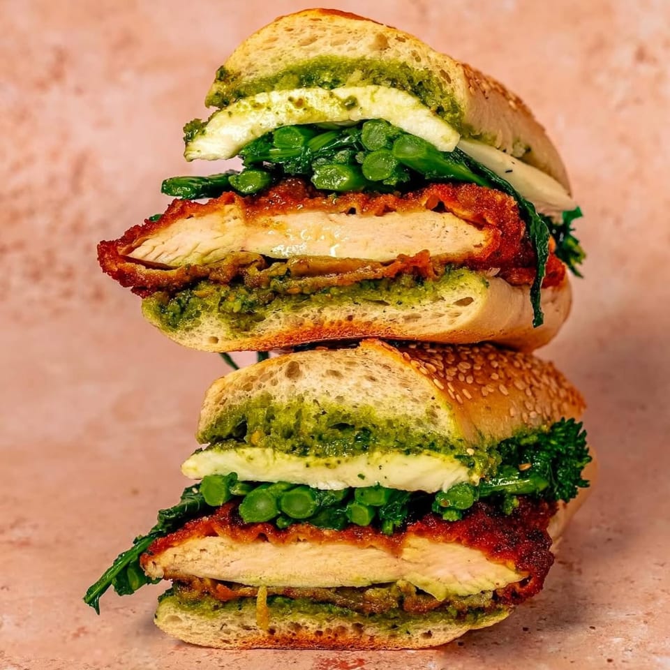 Two halves of a Nana's Bagel sandwich stacked, filled with chicken, pesto, cheese, and greens.