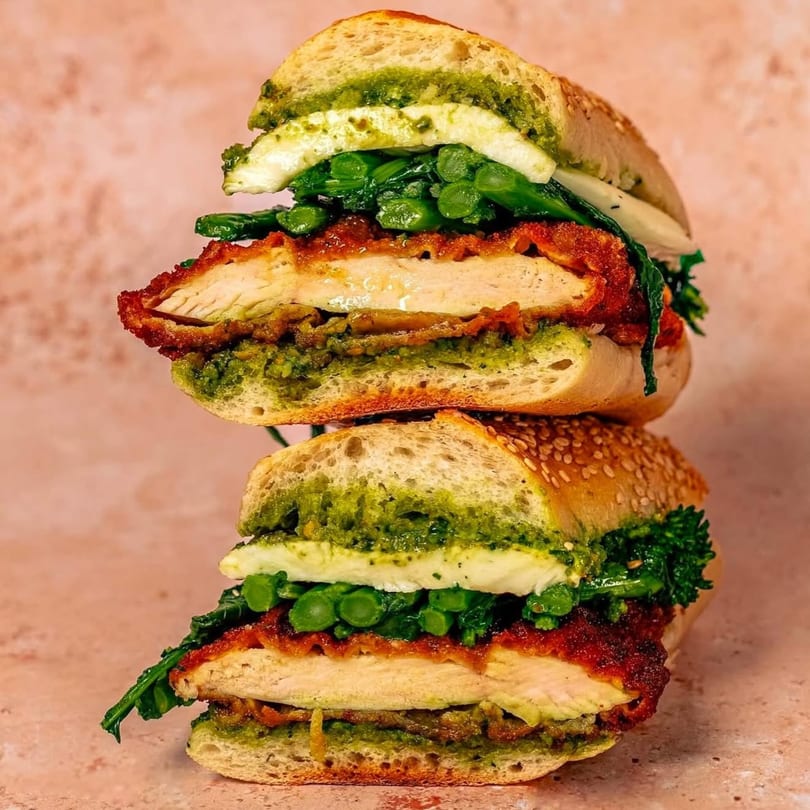 Two halves of a Nana's Bagel sandwich stacked, filled with chicken, pesto, cheese, and greens.
