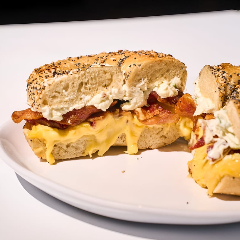 A Nana's Bagel breakfast sandwich with bacon, egg, and cheese, cut in half on a white plate.